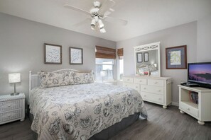 A bedroom with a bed, a dresser, a television, and a ceiling fan.