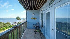 A balcony with a view of the beach and ocean, a table with chairs, and a decorative wall piece. - Fenimore Mill 4B - Pool, Hot Tub, Open Gulf View! (Cedar Key)