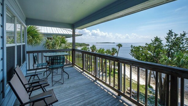 A wooden deck with a table and chairs, overlooking a beach and ocean. - Fenimore Mill 4F - Open Gulf View, Pool, Hot Tub! (Cedar Key)