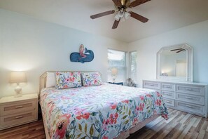 Un dormitorio con cama, mesitas de noche, cómoda, ventilador de techo y un adorno en la pared.