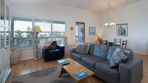 A living room with a sofa, coffee table, and a dining area with chairs and a table. - Fenimore Mill 4F - Open Gulf View, Pool, Hot Tub! (Cedar Key)