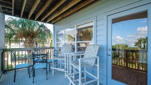 A covered patio with outdoor furniture, a palm tree, and a view of the surrounding area. - Fenimore Mill 7A - Beautiful View, Pool, Hot Tub! (Cedar Key)