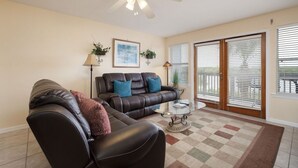 A living room with a brown leather sofa, a glass coffee table, and a ceiling fan. - Fenimore Mill 8B - Boat Parking, Pool, Hot Tub! (Cedar Key)