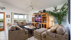 Ein geräumiges Wohnzimmer mit einer Sofagarnitur, einem Couchtisch, einem Bücherregal und einer großen Pflanze.