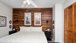 Ein Schlafzimmer mit einem großen Bett, einem Holz-Kopfteil, gerahmten Kunstwerken, Nachttischlampen und einem Deckenventilator.