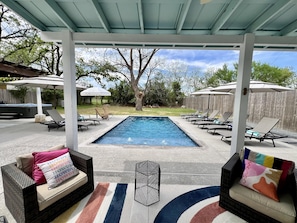 A covered outdoor pool area with lounge chairs and umbrellas, a hot tub, and a wooden fence in the background.