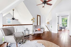 A spacious loft with high ceilings, a wooden staircase, and a large window offering a view of greenery.