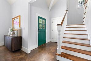 A hallway with a teal door, a staircase with wooden steps, and a dark brown floor.