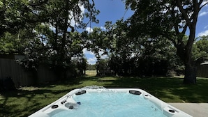 Un jacuzzi en un patio trasero con árboles y una valla de madera.