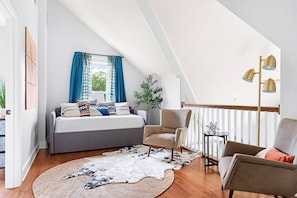 A bedroom with a bed, two chairs, a small table, a lamp, and a window with curtains.