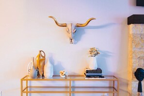 A wall-mounted horn above a console table with decorative vases, books, and a vase with flowers.