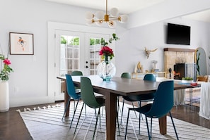 A dining area with a wooden table, teal chairs, a vase with flowers, a fireplace, and a mounted TV.