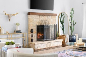 A living room with a stone fireplace, a mounted TV, and a variety of decor items including plants and books.