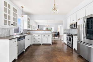 A spacious kitchen with white cabinetry, a marble countertop, stainless steel appliances, and a central island.