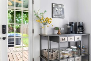A kitchen area with a coffee station, a decorative sign, and a view of a backyard through a glass door.