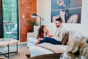 A living room with a white couch, a coffee table, and a brick wall.