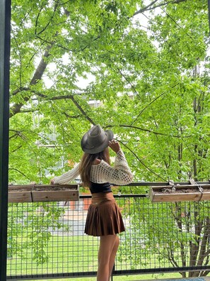 A person standing on a balcony with a view of a green park and trees.