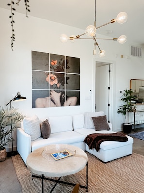 A modern living room with a white sofa, a round coffee table, and a large abstract painting on the wall. - S Lamar Loft• King Bed •Tree Balcony• Pets• Zilker (Austin)