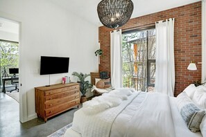 A bedroom with a large bed, a wooden dresser, a TV, and a window with curtains.