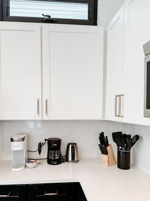 A modern kitchen with white cabinets, a coffee maker, a kettle, and a knife block.