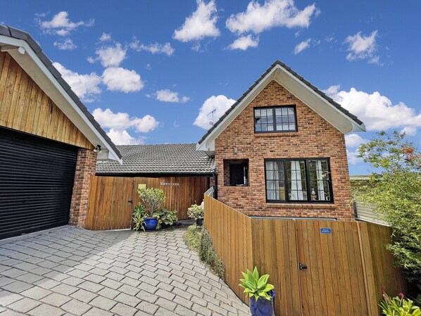 A two-story house with a brick facade, a wooden fence, and a paved driveway. - Riversong - Pambula Beach (Pambula Beach)