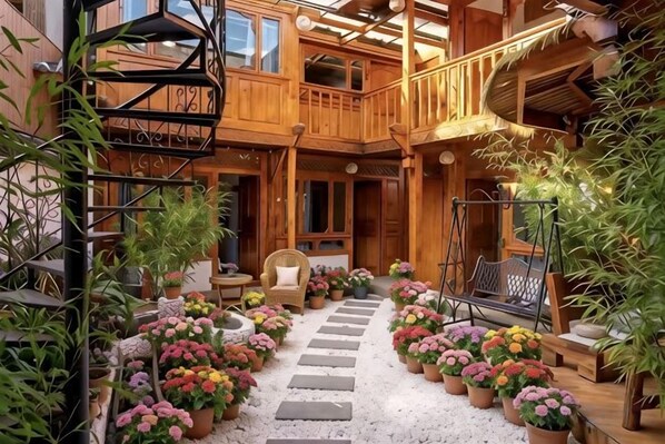 A wooden multi-level building with a central staircase, outdoor seating area, and potted plants.
