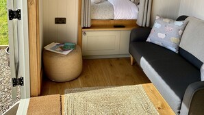 A cozy interior with a bed, a sofa, a small round ottoman, and a door leading outside.