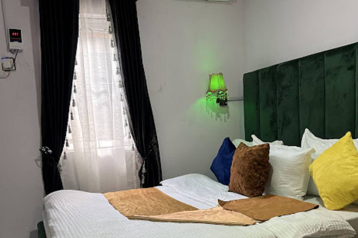 Un dormitorio con una cama tapizada en verde, ropa de cama blanca y una lámpara verde montada en la pared.