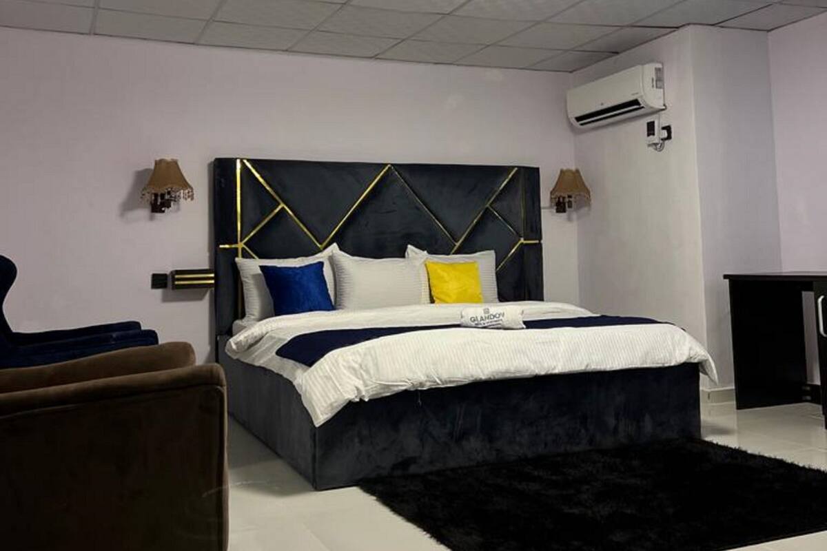Un dormitorio moderno con una cama grande, una alfombra negra, una silla y un equipo de aire acondicionado en la pared.