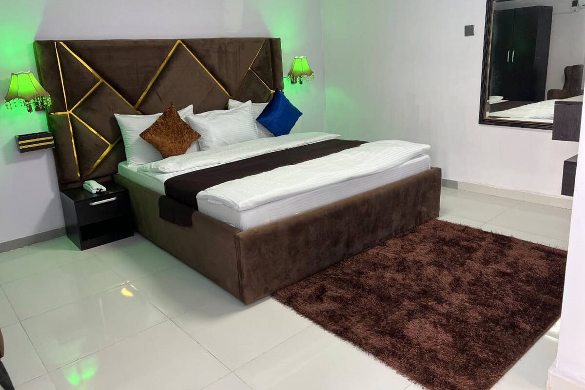 Un dormitorio moderno con una cama grande, cabecera con diseños geométricos, dos lámparas de noche y una alfombra marrón mullida.