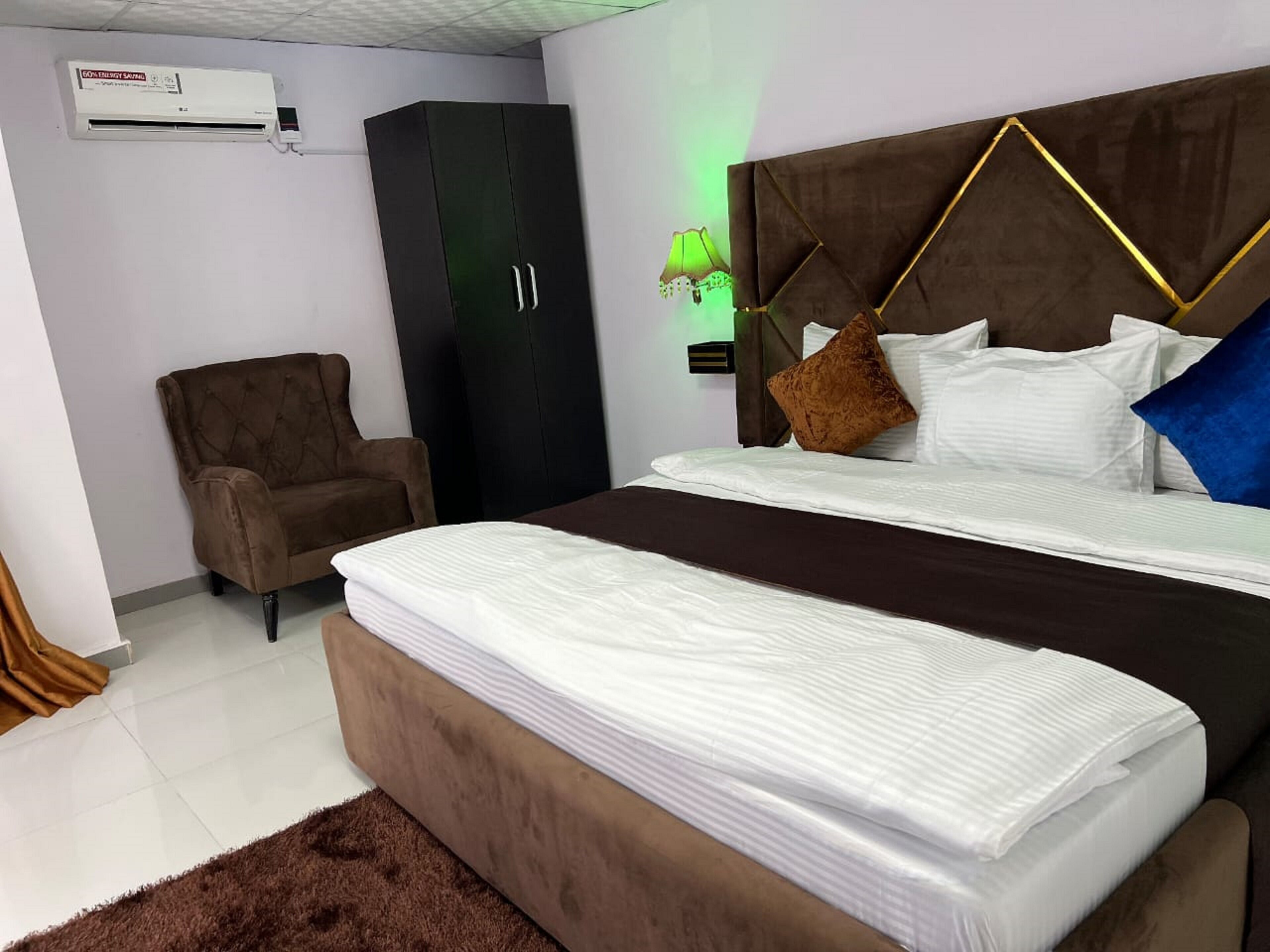 Un dormitorio con cama doble, un sillón marrón, un armario negro y una lámpara de pared con luz verde.