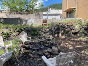 A patio area with a fire pit, white Adirondack chairs, and a stone wall.
