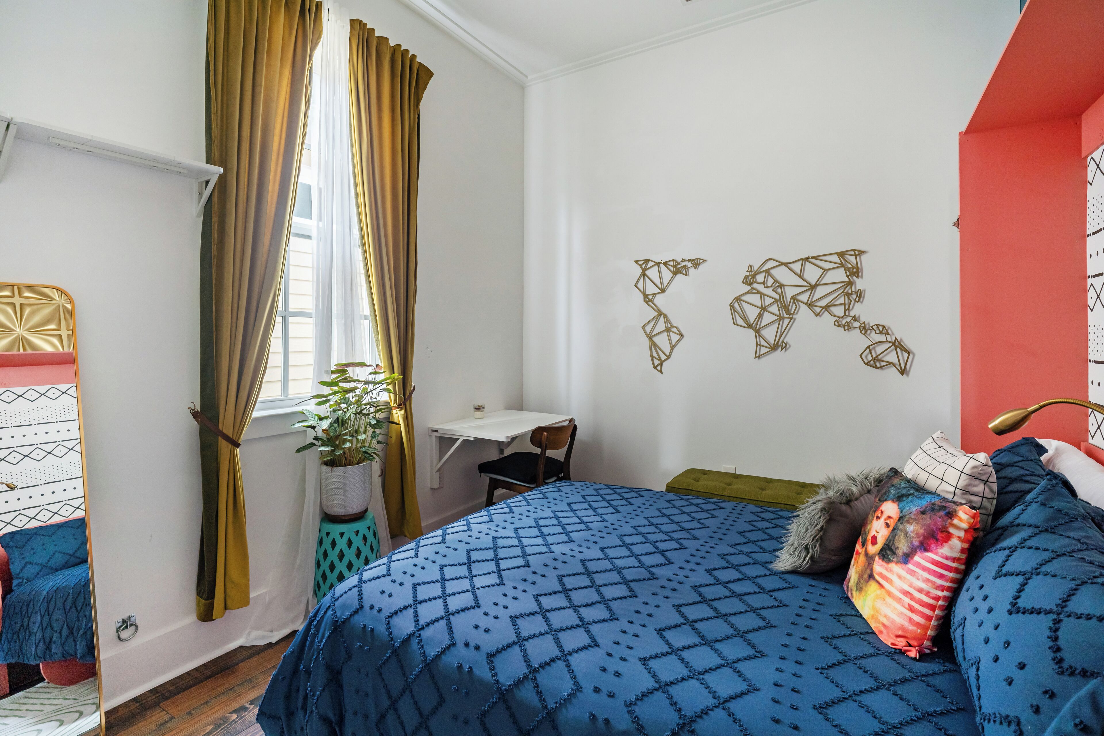 A bedroom with a bed, a desk, a chair, a window with curtains, and wall art.