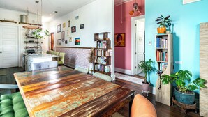 A dining area with a wooden table, chairs, and a green sofa. There is a kitchen in the background with a white door. - Chic Surroundings in Uptown New Orleans! (New Orleans)