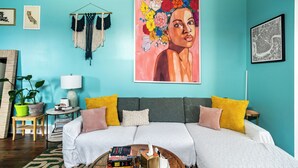 A teal-walled living room with a sofa, cushions, a coffee table with books, a lamp, a plant, and a fireplace. - Chic Surroundings in Uptown New Orleans! (New Orleans)