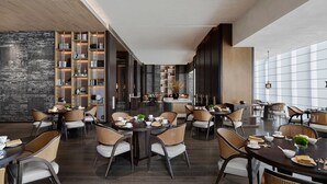 Een moderne eetruimte met meerdere tafels en stoelen, een centraal eiland en een boekenkast met boeken en decoratieve objecten.