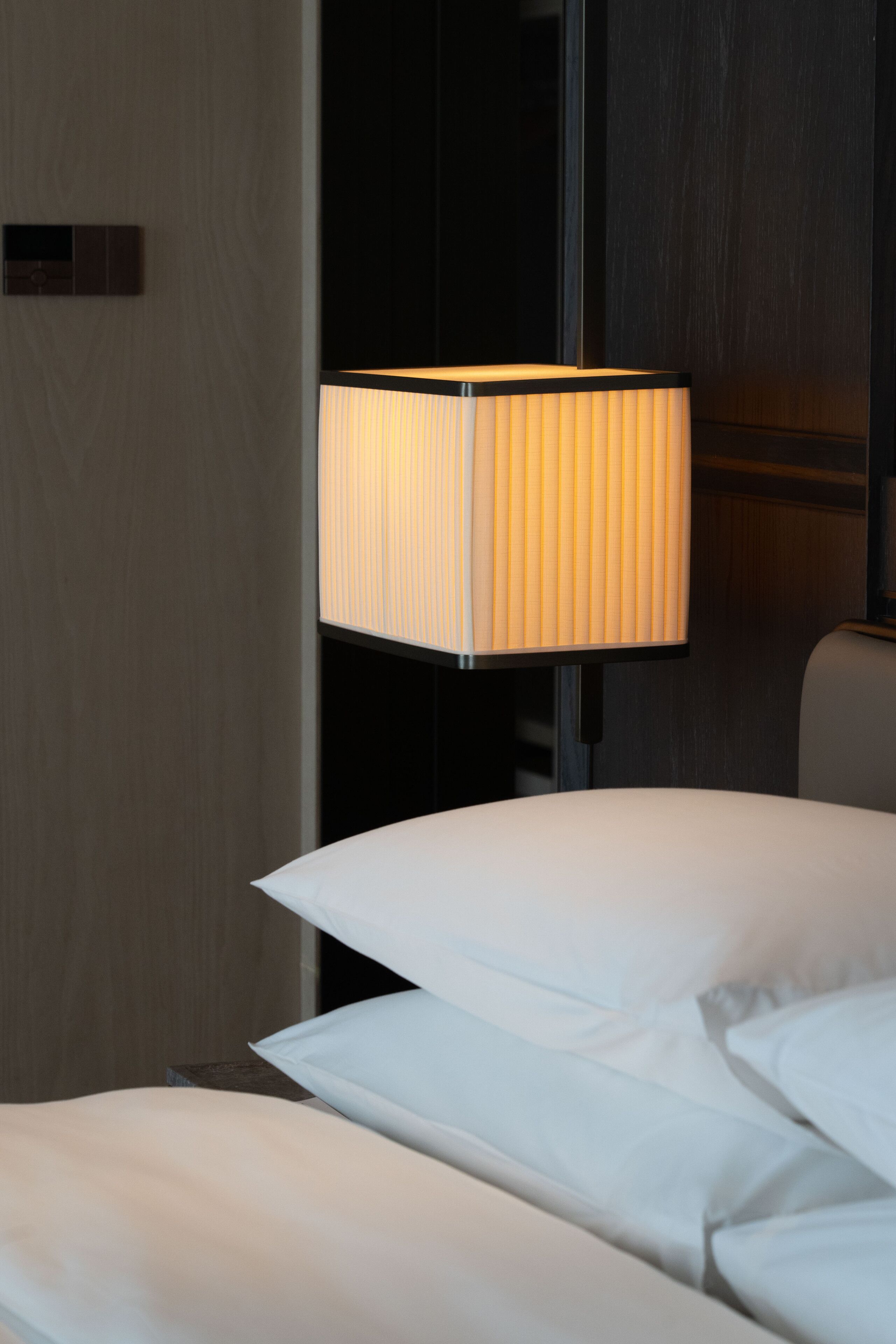 Una habitación de hotel moderna con una lámpara de noche, una puerta de madera y una cama blanca.