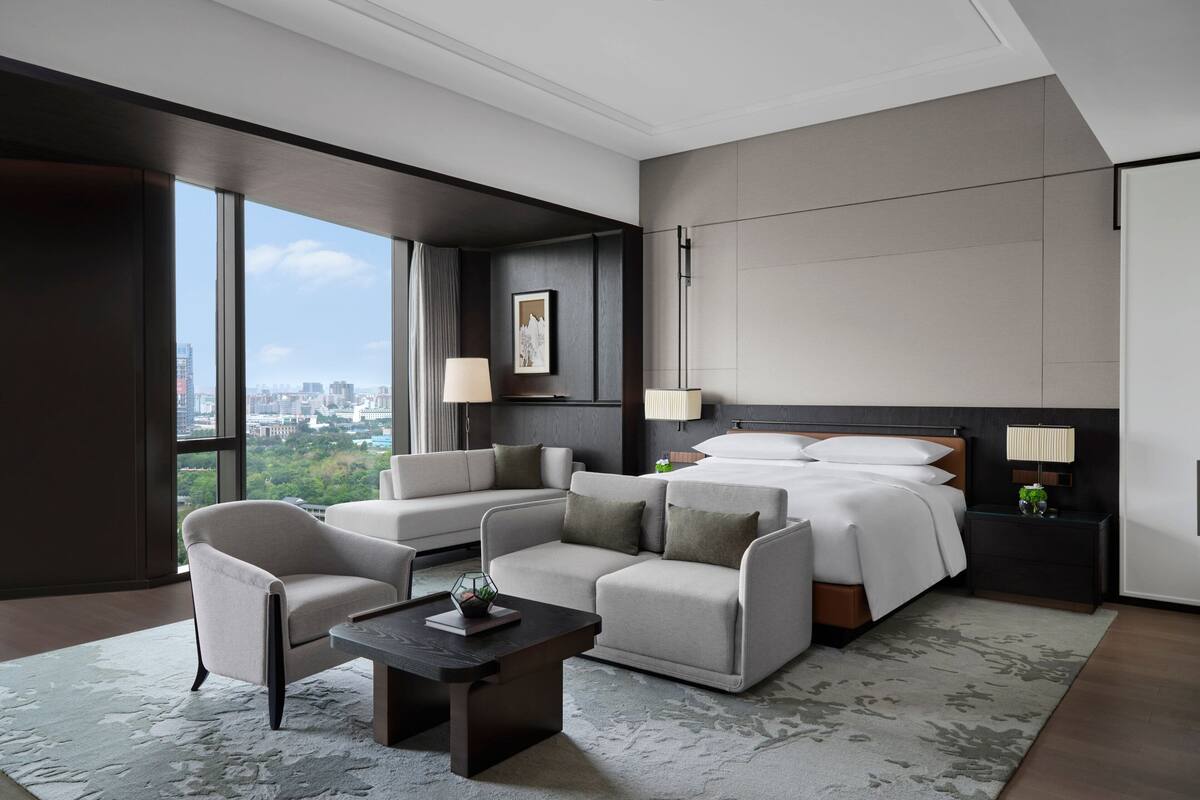 Une chambre d’hôtel moderne avec un grand lit, deux canapés, une table basse et une vue sur la ville.