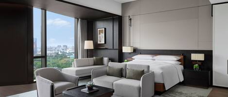 A modern hotel room with a large bed, two sofas, a coffee table, and a city view.