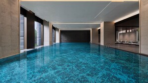 Een groot binnenzwembad met een blauwe, gestructureerde vloer, omringd door muren en een plafond met inbouwverlichting.