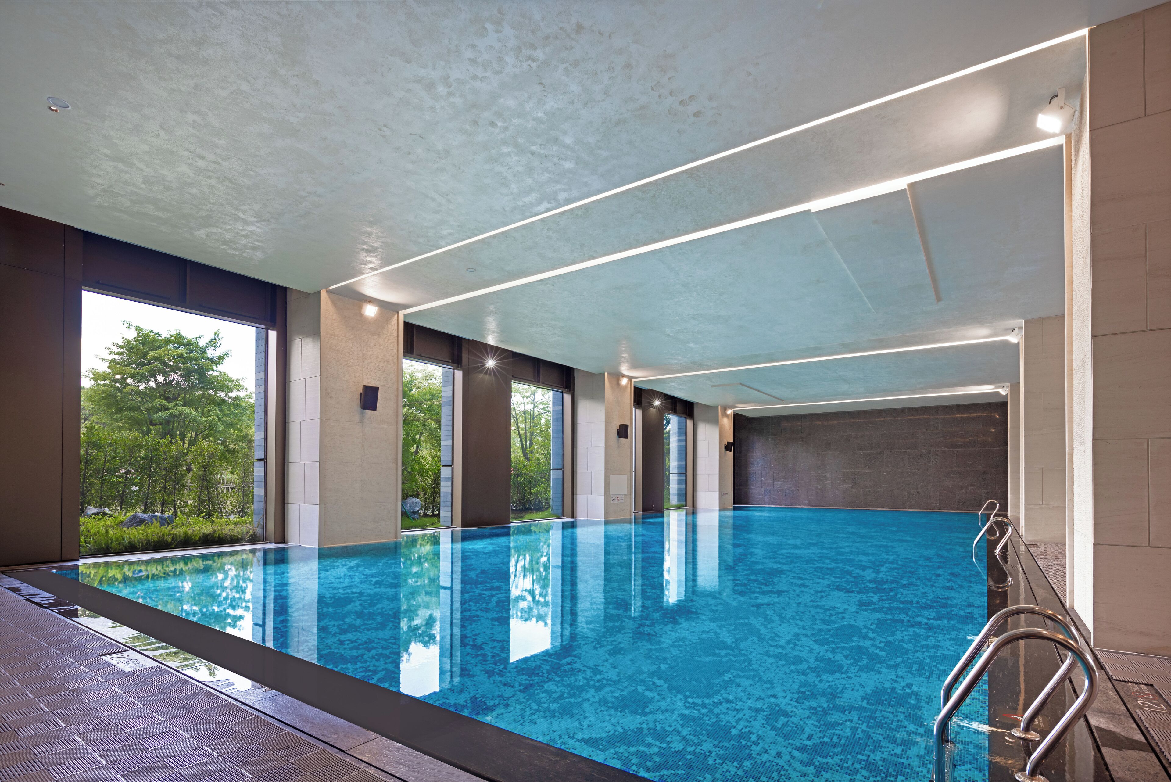 En inomhuspool med kristallklart blått vatten, stora fönster och en modern takdesign.