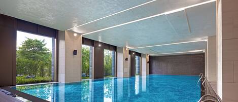 Una piscina interior con agua azul cristalina, ventanas amplias y un diseño moderno en el techo.