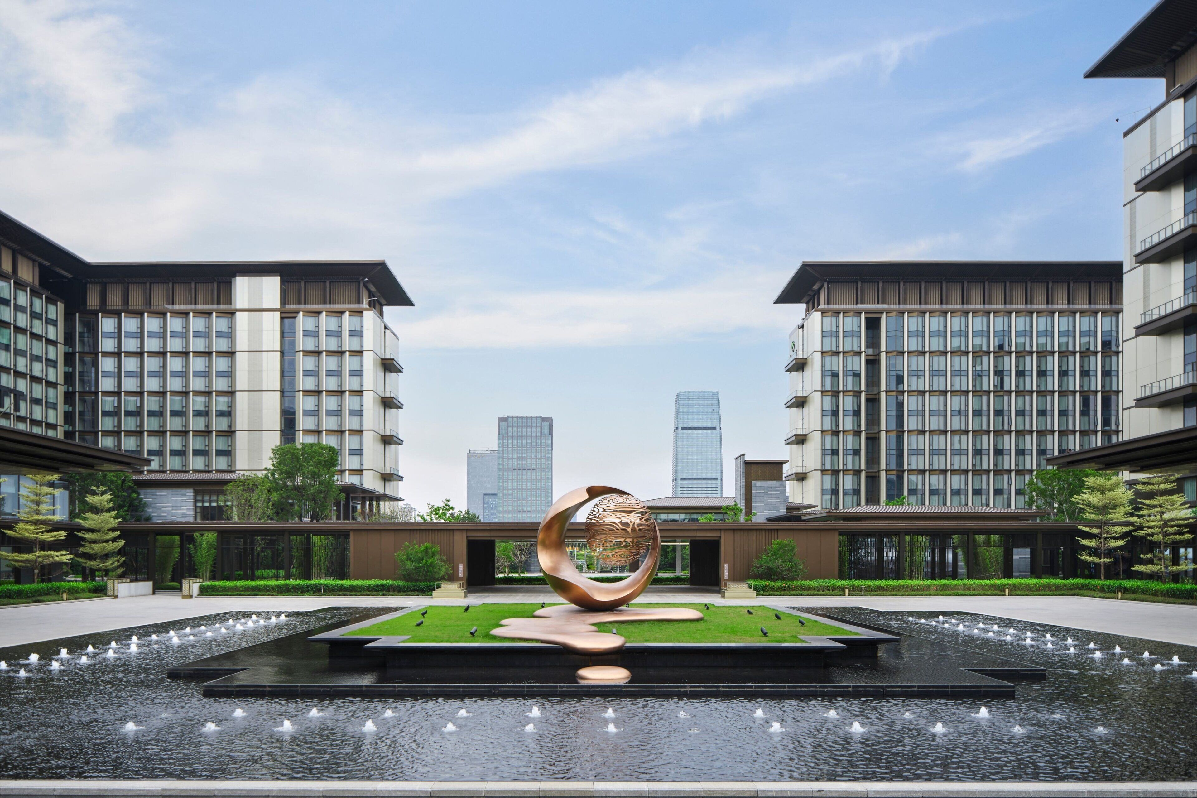 A modern building with a central water feature and a large metallic sculpture.