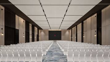 Un salón de conferencias con filas de sillas blancas, una alfombra estampada y una pantalla grande al frente.
