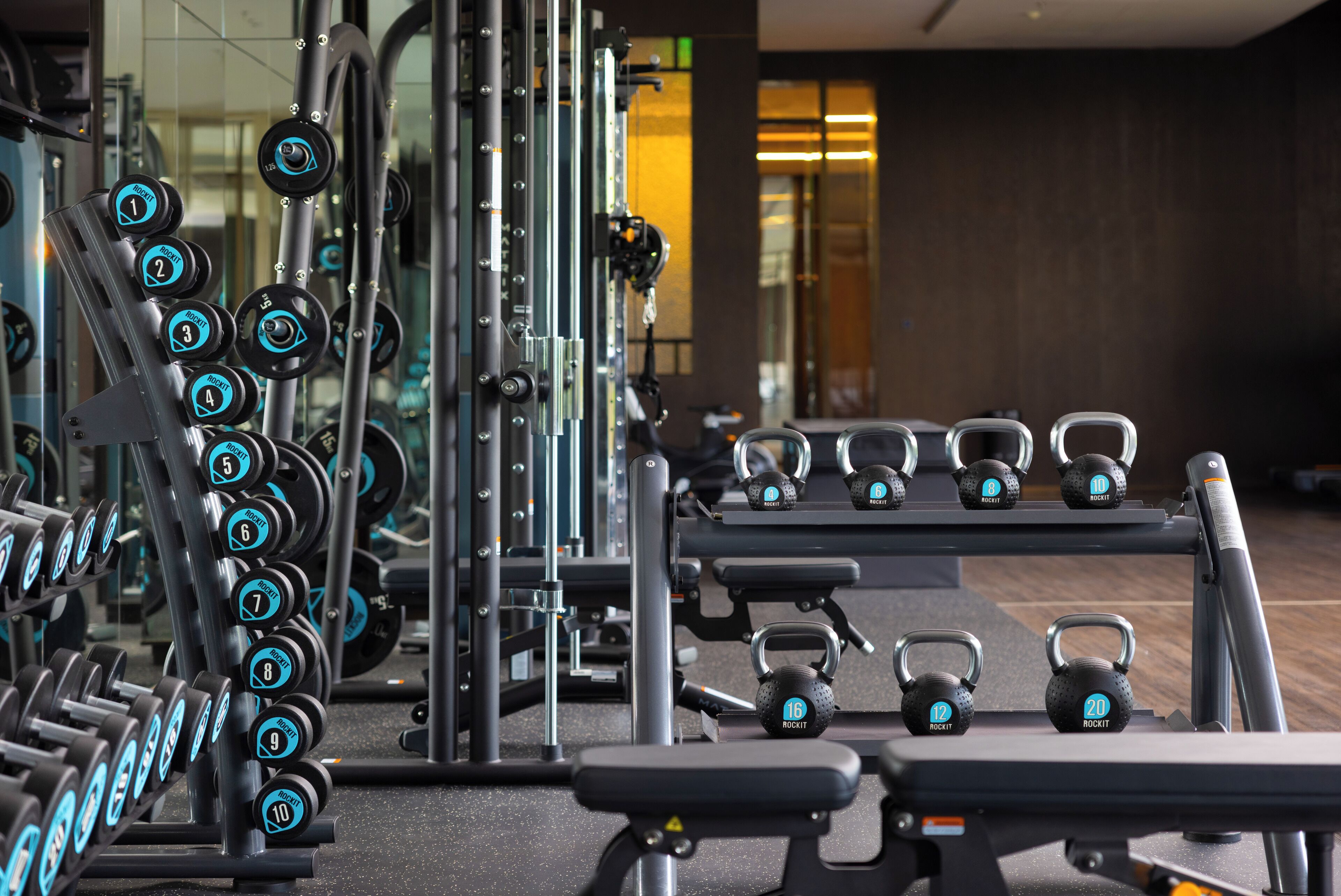 A gym with various weightlifting equipment, including dumbbells and kettlebells, arranged on racks and benches.