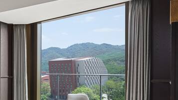 A modern hotel room with a large window offering a view of a cityscape and mountains.