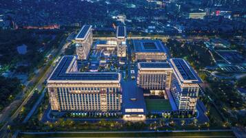 An aerial view of a modern building complex with multiple high-rise structures, surrounded by greenery and roads.