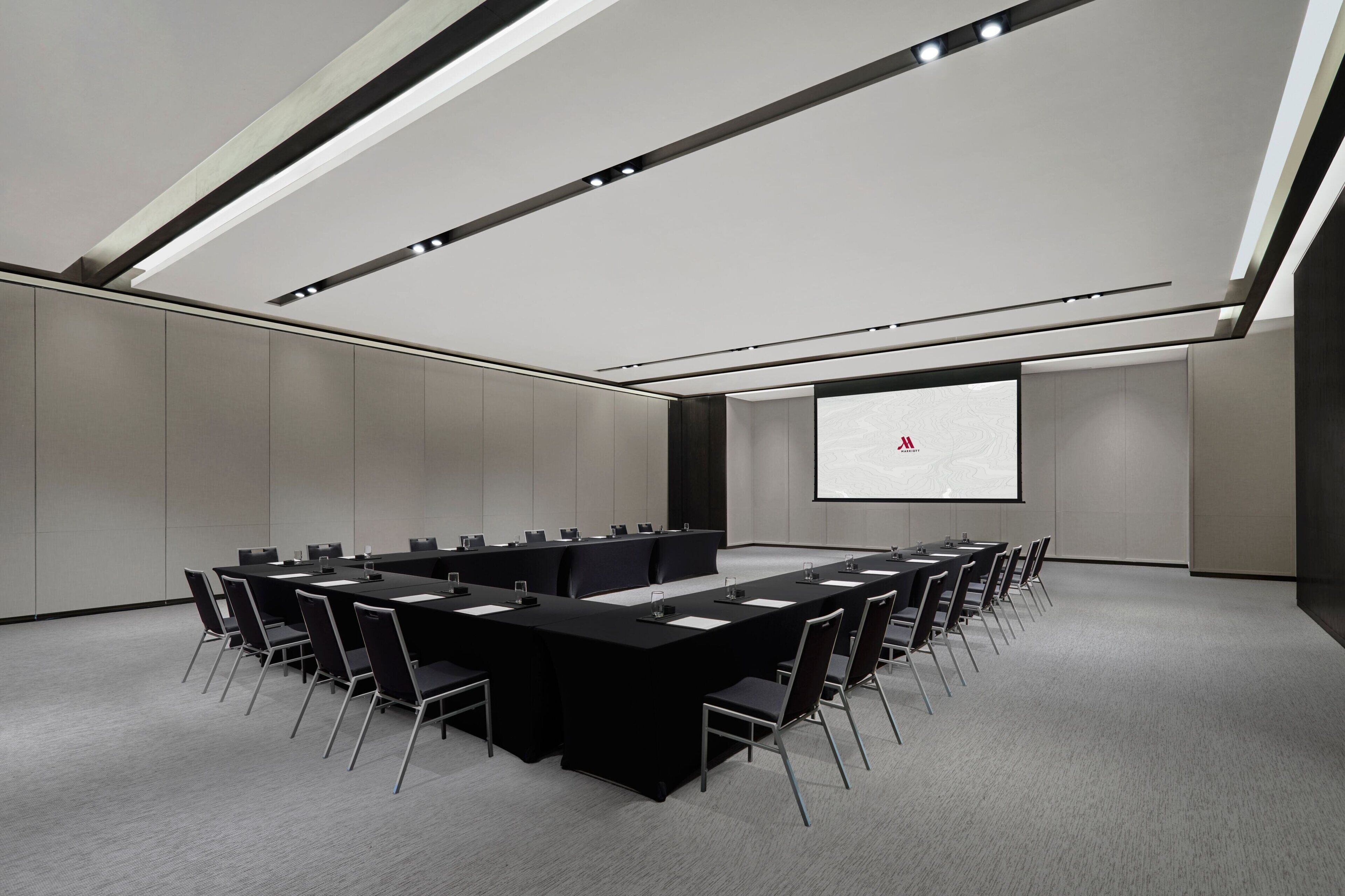 Un salón de conferencias con una larga mesa, sillas, una pantalla de proyector y una pantalla de presentación.