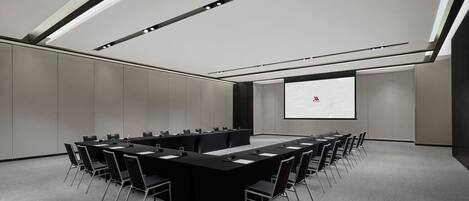 Un salón de conferencias con una larga mesa, sillas, una pantalla de proyector y una pantalla de presentación.