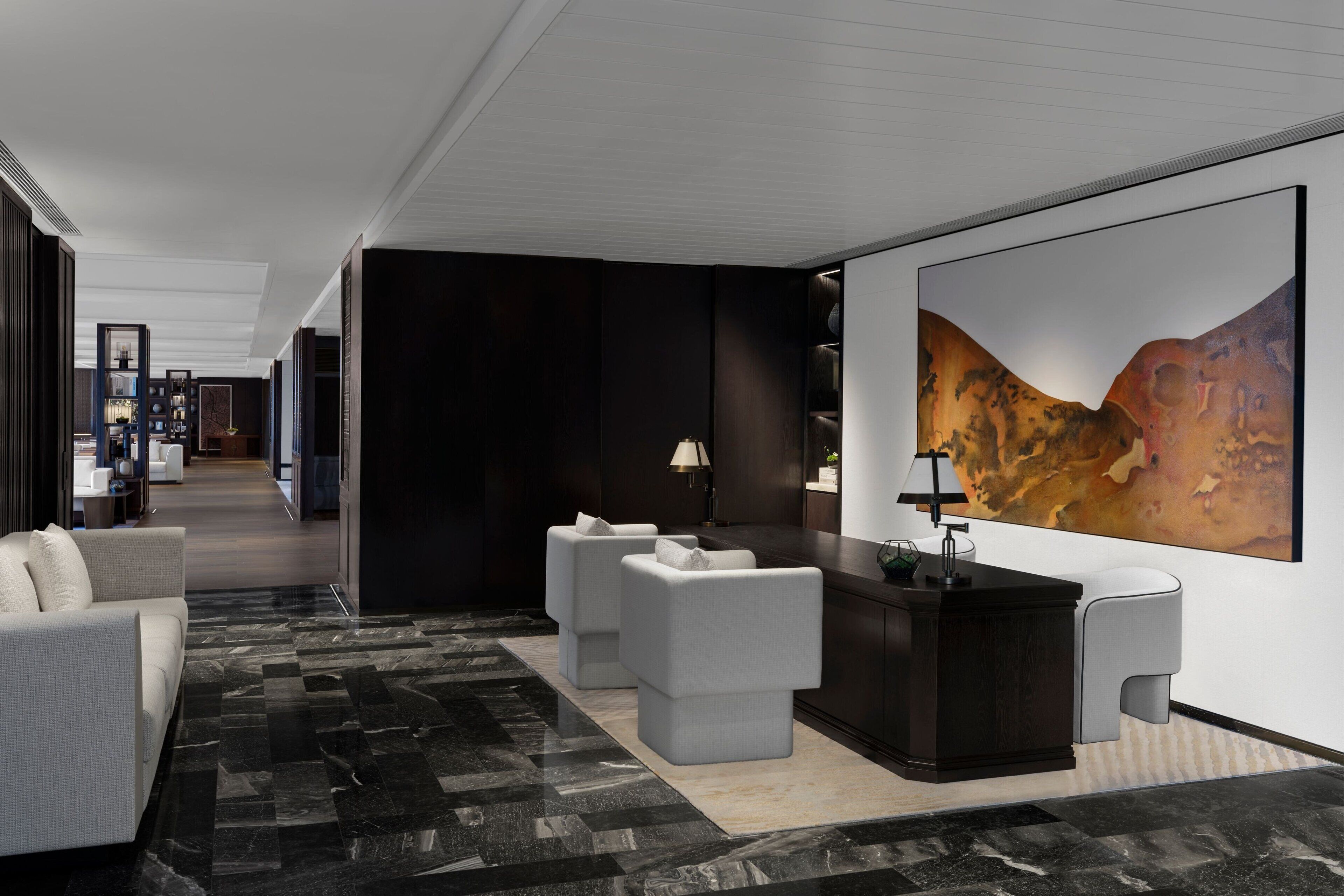 A modern hotel lobby with a dark wood reception desk, white sofas, and a large abstract painting on the wall.